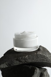 Face cream in jar on stones against light background