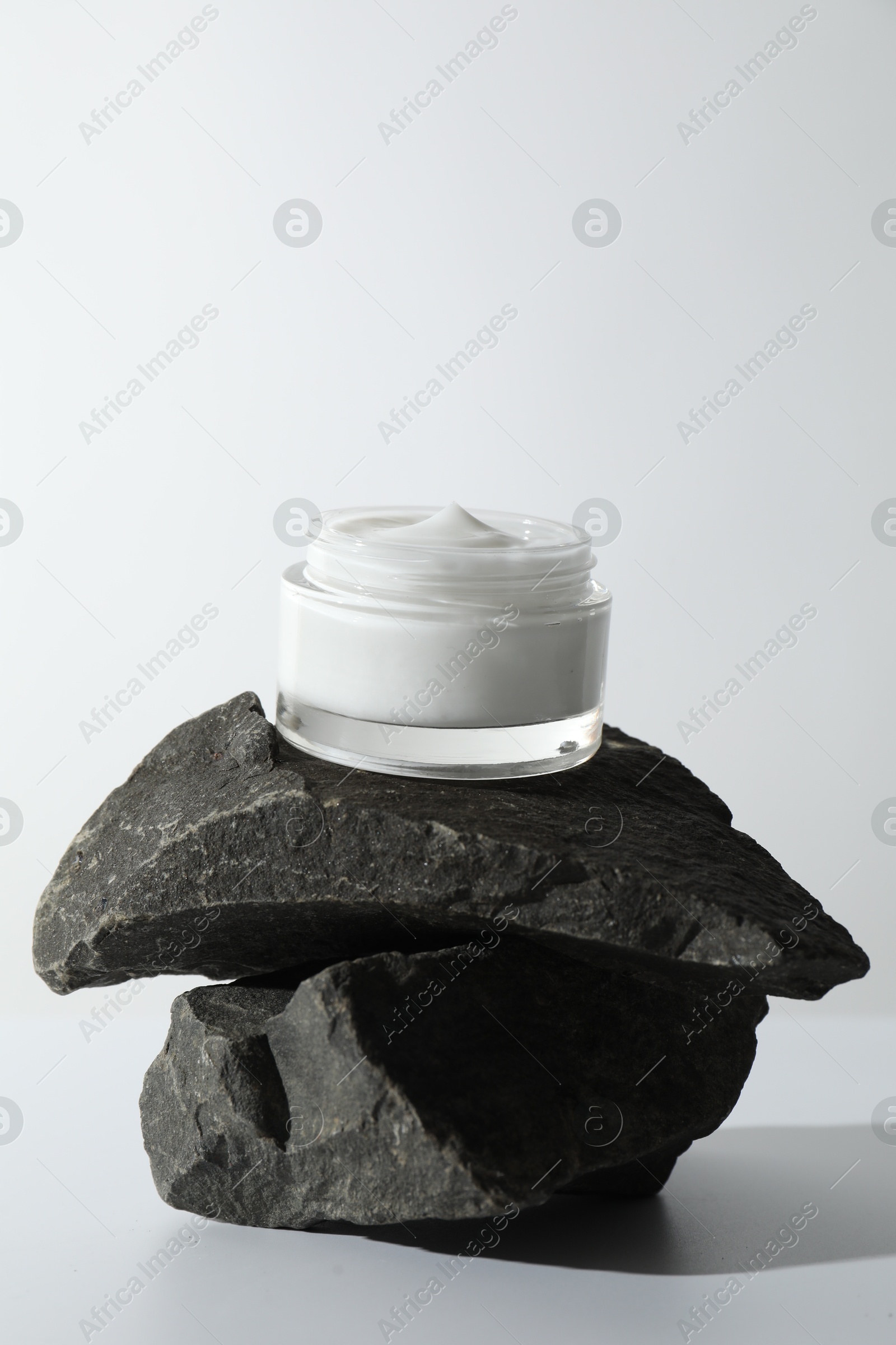 Photo of Face cream in jar on stones against light background