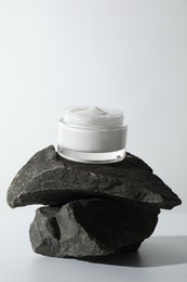 Face cream in jar on stones against light background