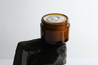 Face cream in jar on stone against light background