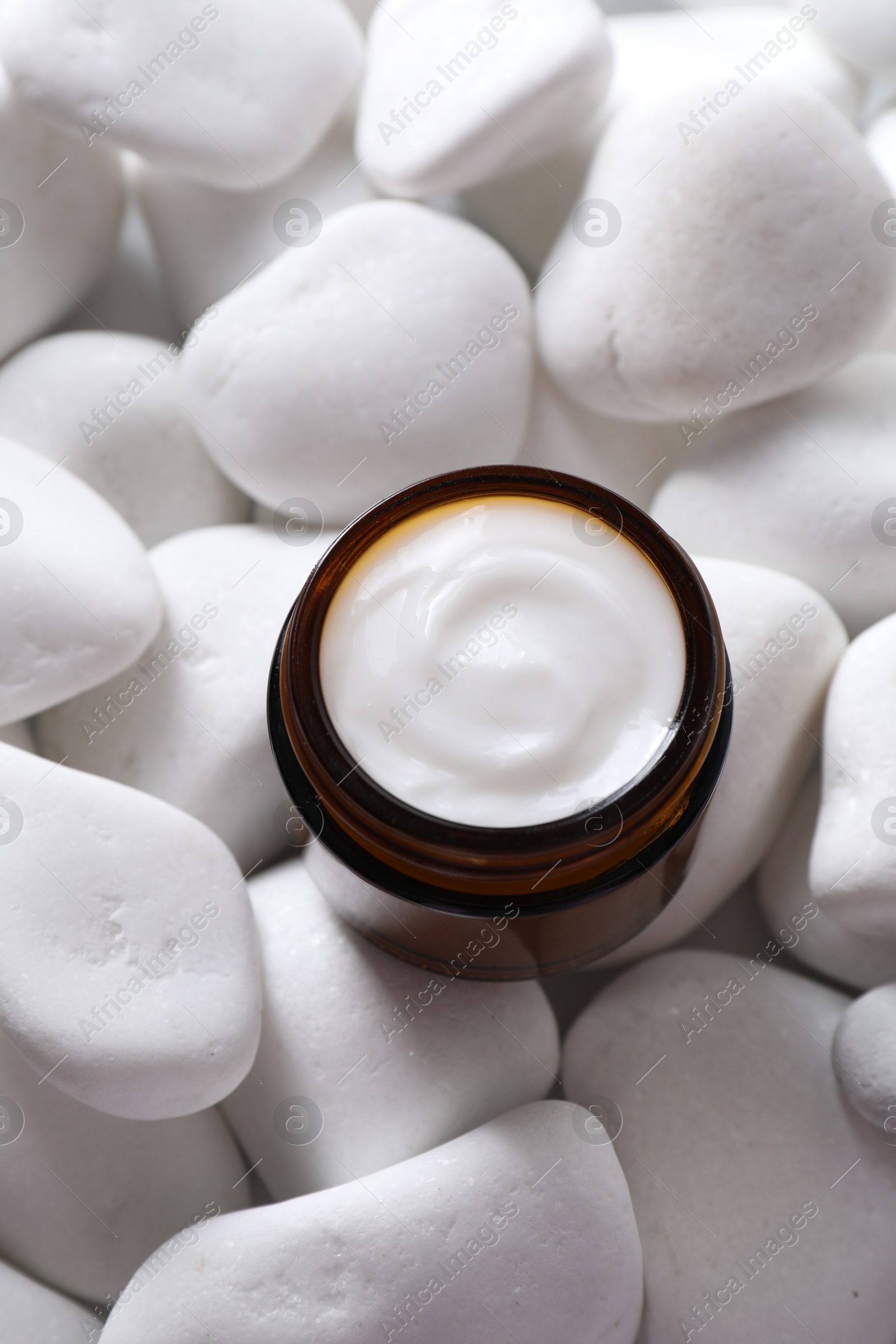 Photo of Face cream in jar on white stones, top view. Cosmetic product