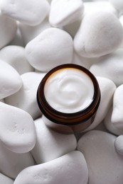 Face cream in jar on white stones, top view. Cosmetic product