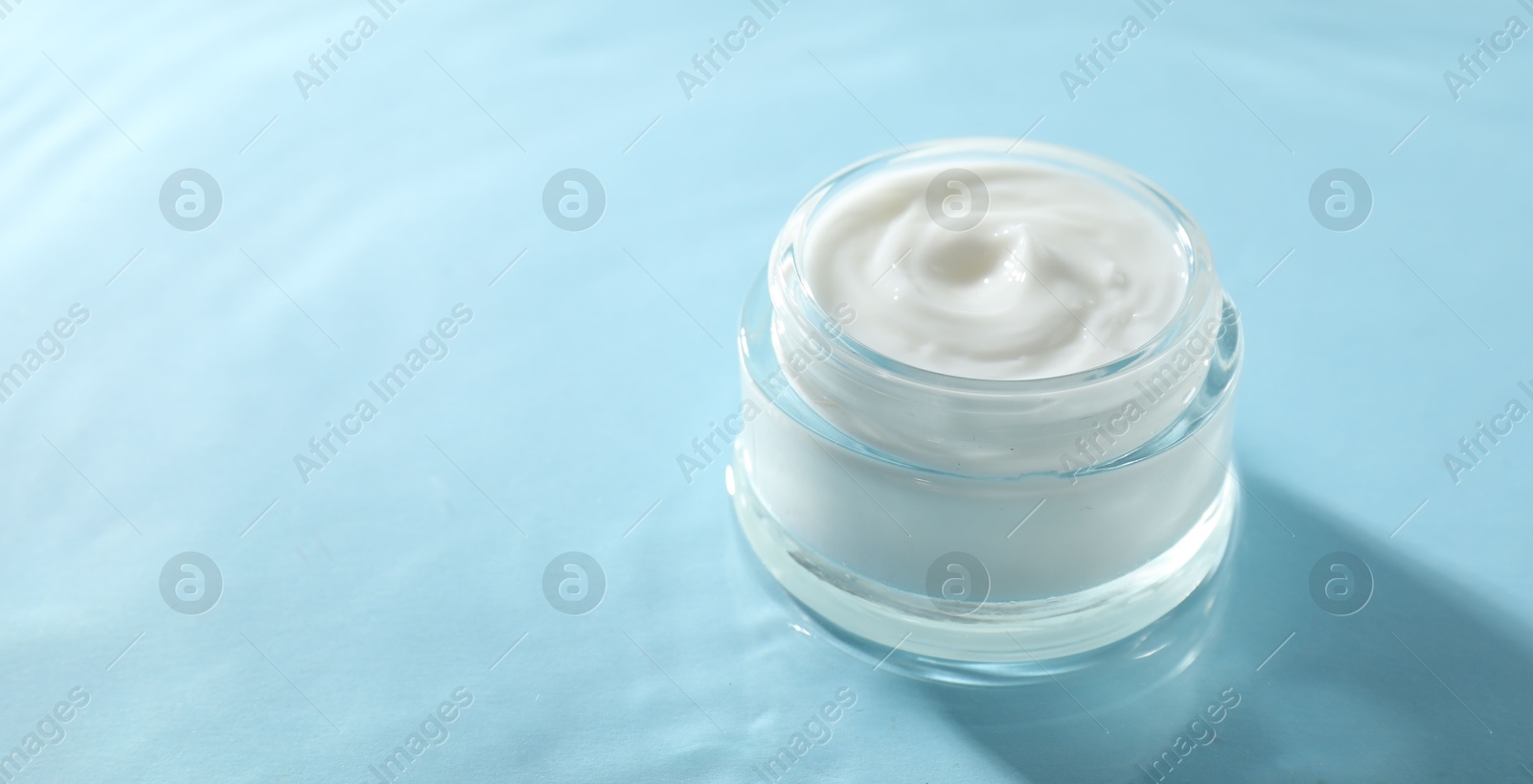 Photo of Jar with face cream in water on light blue background, space for text