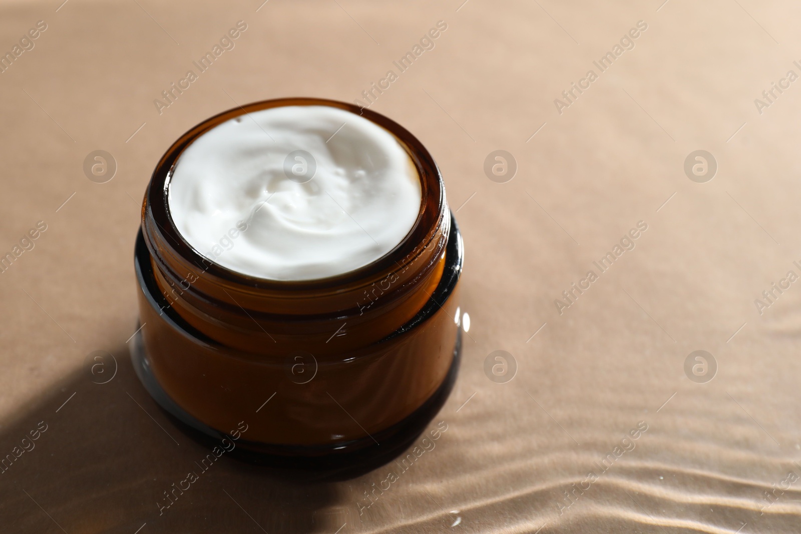 Photo of Jar with face cream in water on beige background, closeup. Space for text