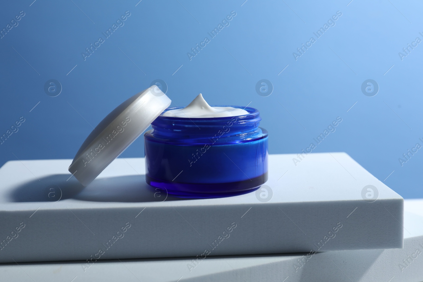 Photo of Stylish presentation of face cream in jar against light blue background