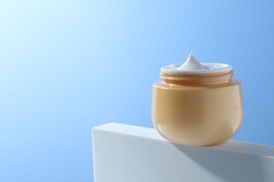 Face cream in jar against light blue background, closeup. Space for text