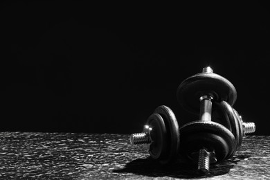 Photo of Two barbells on grey textured table against black background. Space for text