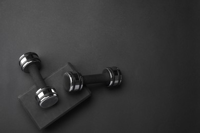 Photo of Two dumbbells and yoga block on black background, flat lay. Space for text