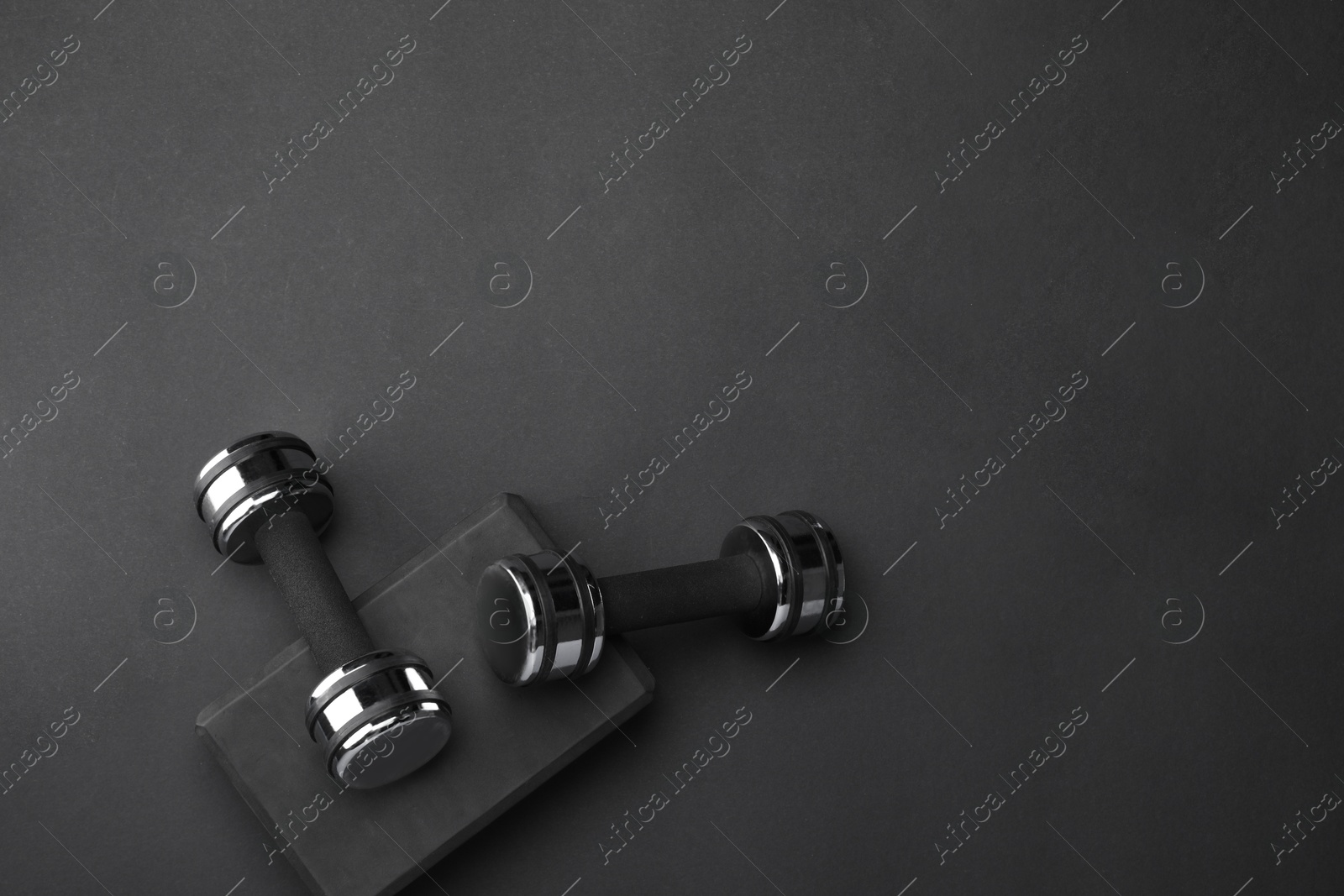 Photo of Two dumbbells and yoga block on black background, flat lay. Space for text