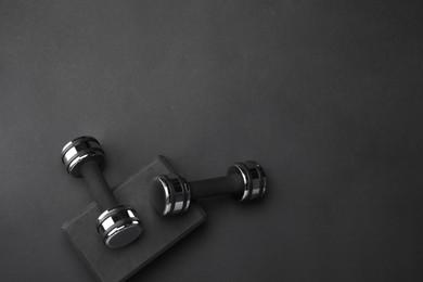 Two dumbbells and yoga block on black background, flat lay. Space for text