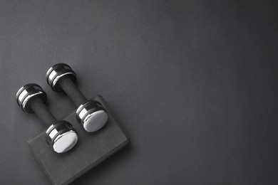 Two dumbbells and yoga block on black background, flat lay. Space for text