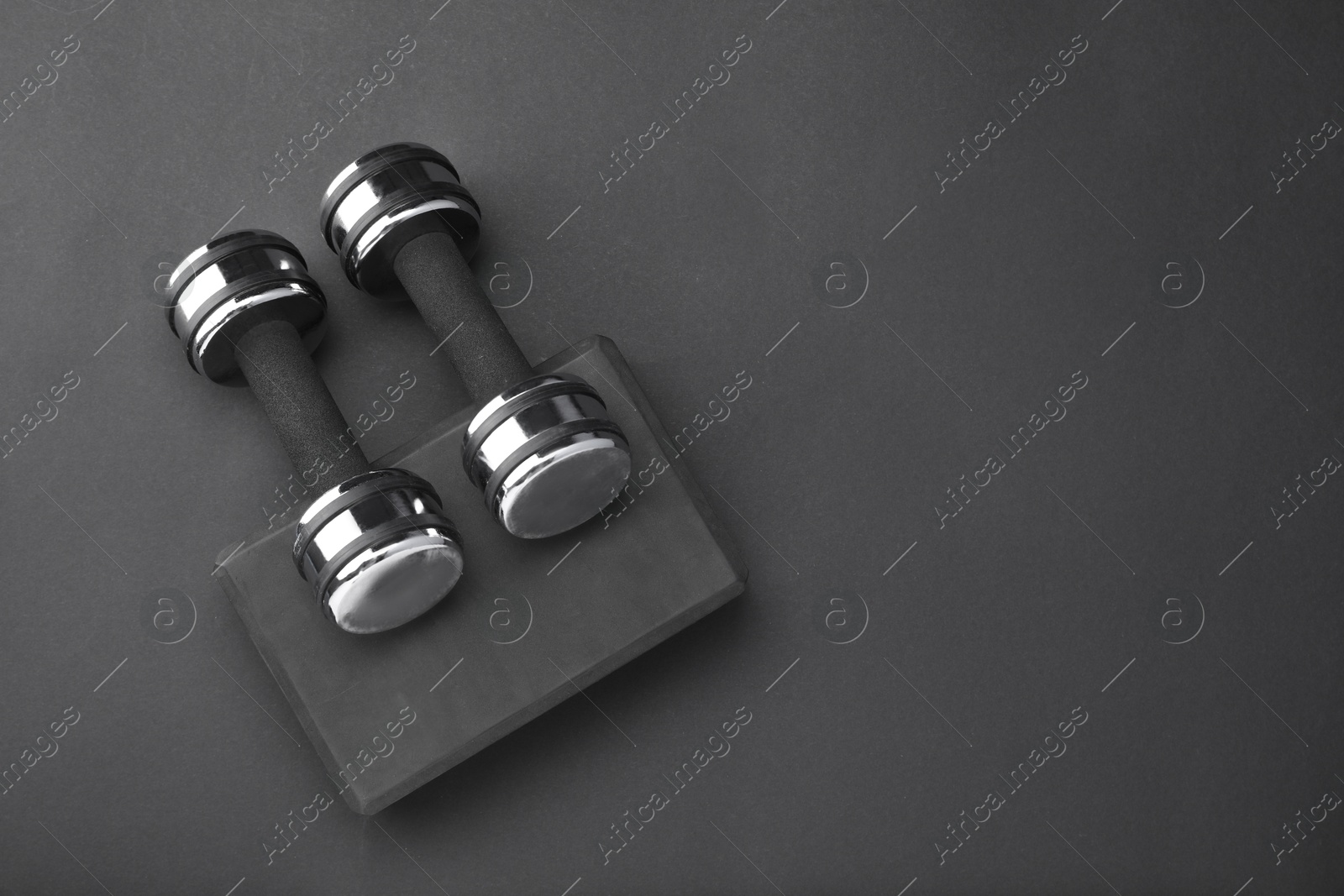 Photo of Two dumbbells and yoga block on black background, flat lay. Space for text