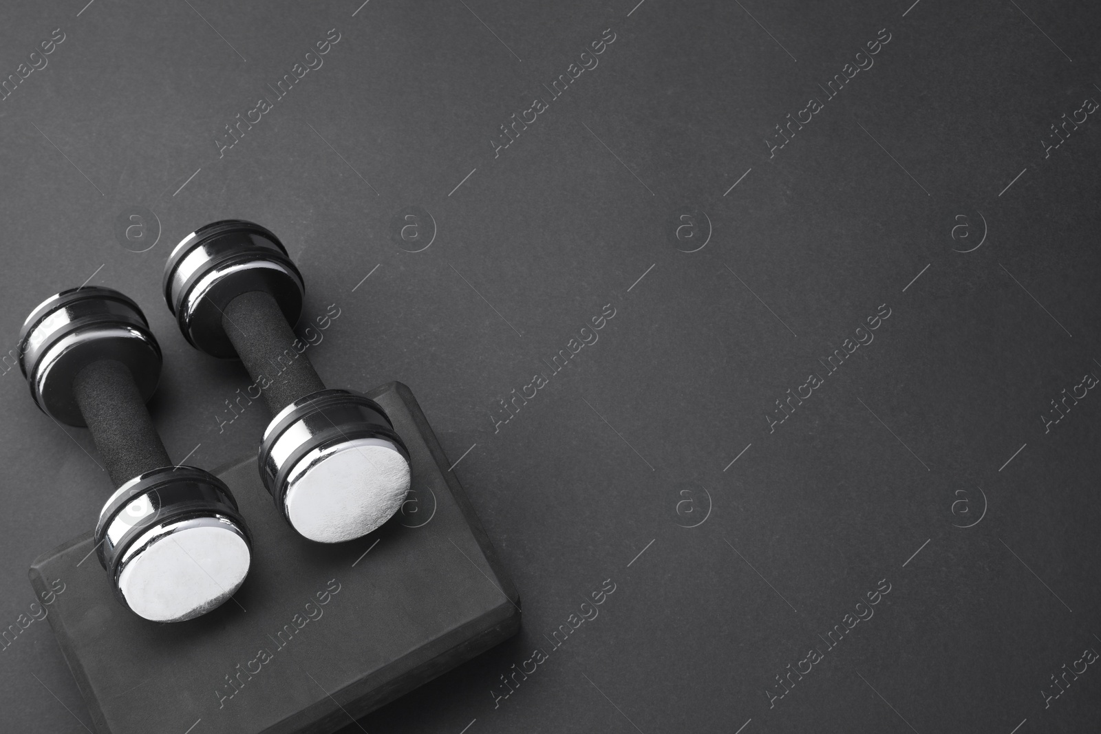 Photo of Two dumbbells and yoga block on black background, flat lay. Space for text