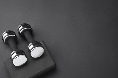 Two dumbbells and yoga block on black background, flat lay. Space for text