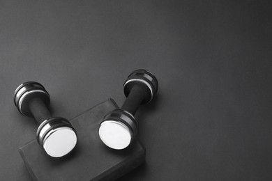 Photo of Two dumbbells and yoga block on black background, above view. Space for text