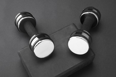 Photo of Two dumbbells and yoga block on black background, above view