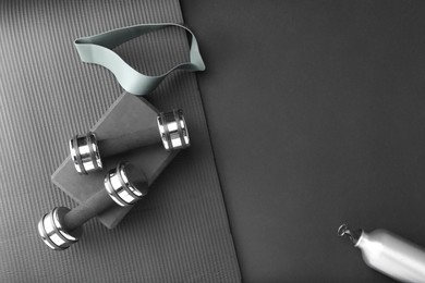 Dumbbells, yoga block, mat, thermo bottle and fitness elastic band on black background, flat lay. Space for text