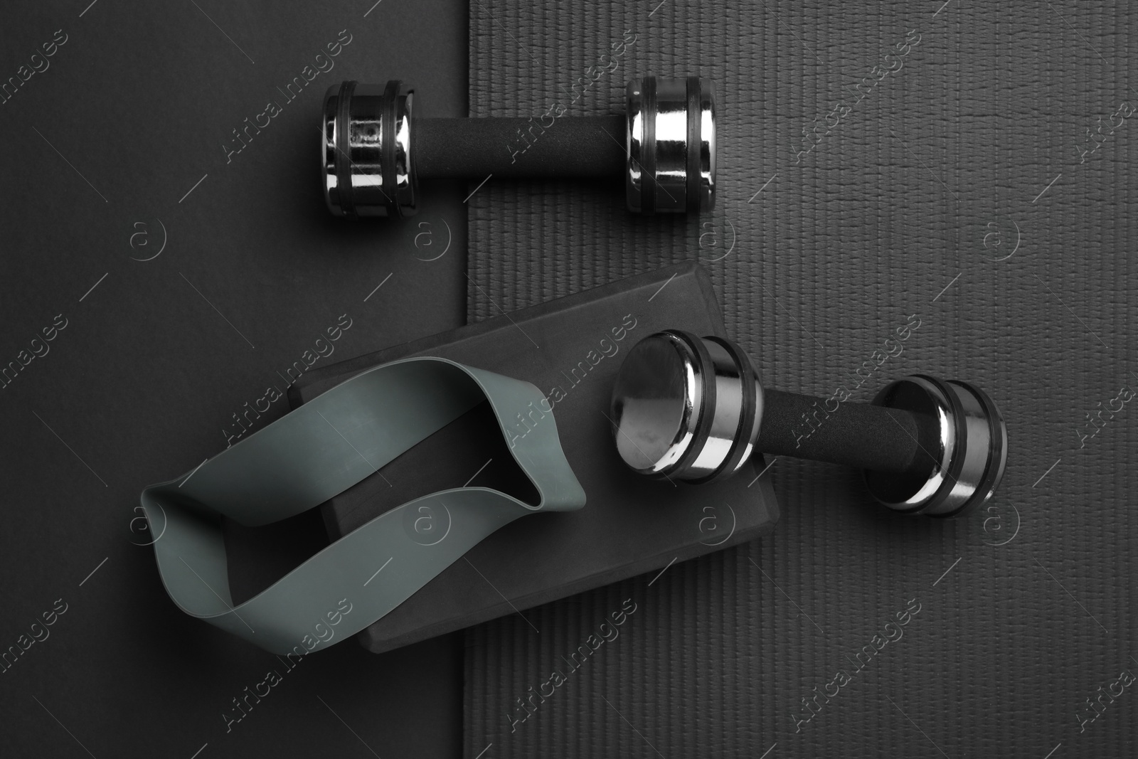 Photo of Dumbbells, yoga block, mat and fitness elastic band on black background, flat lay