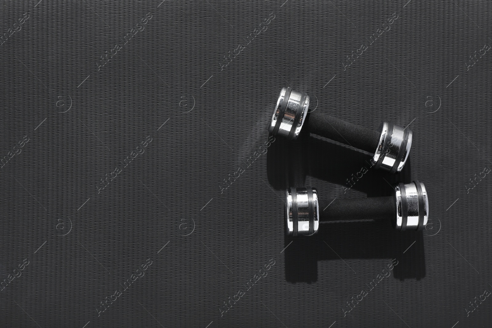 Photo of Dumbbells on black yoga mat, top view. Space for text