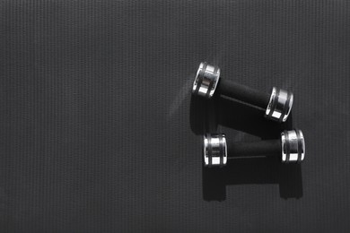 Dumbbells on black yoga mat, top view. Space for text