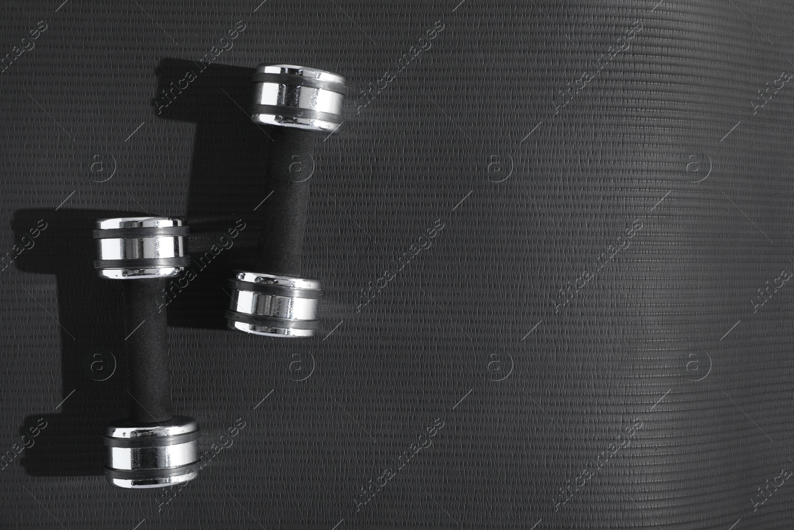 Photo of Dumbbells on black yoga mat, top view. Space for text