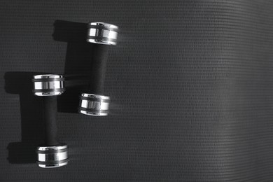 Dumbbells on black yoga mat, top view. Space for text