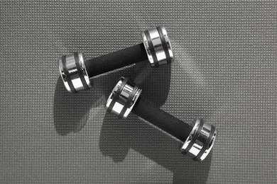 Dumbbells on grey yoga mat, top view