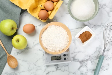 Flat lay composition of kitchen scale with bowl of flour and products on white marble table