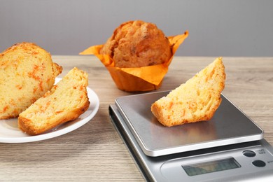 Kitchen scale with piece of muffin on light wooden table, closeup