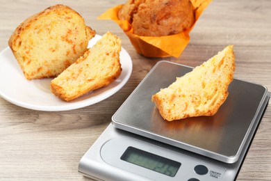 Photo of Kitchen scale with piece of muffin on light wooden table, closeup