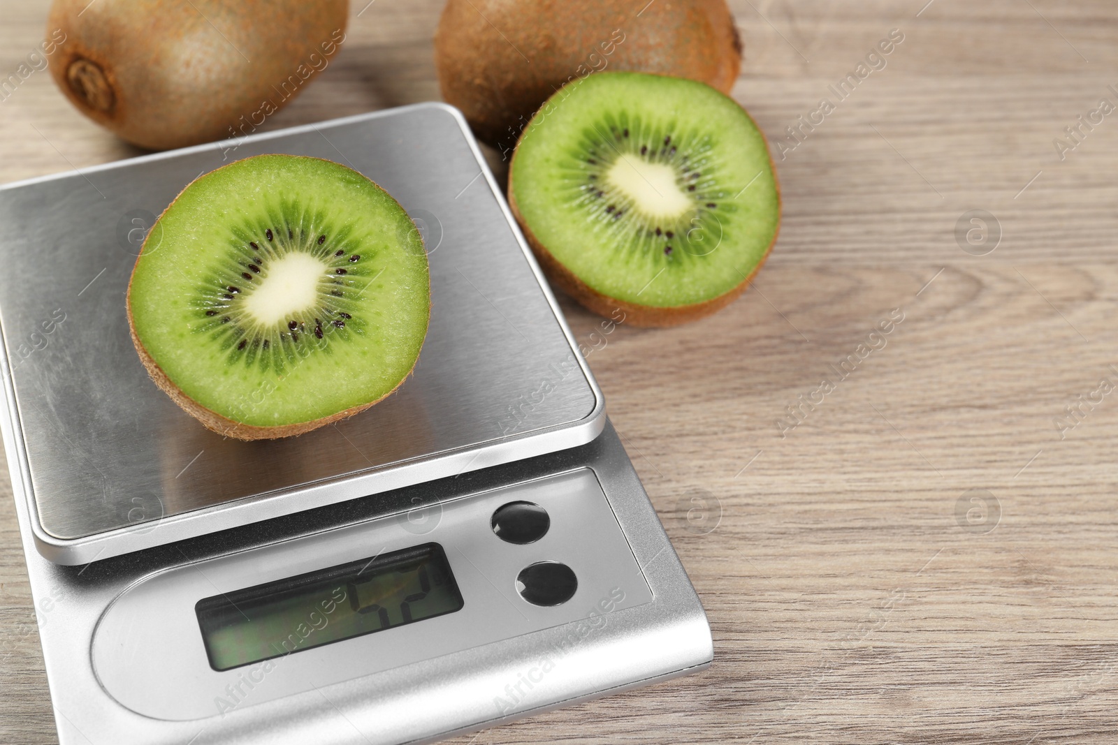 Photo of Kitchen scale with piece of kiwi on light wooden table, closeup. Space for text