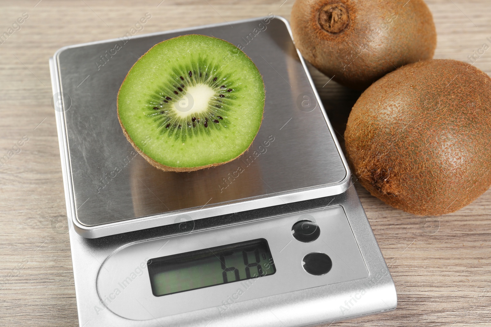 Photo of Kitchen scale with piece of kiwi on light wooden table, closeup