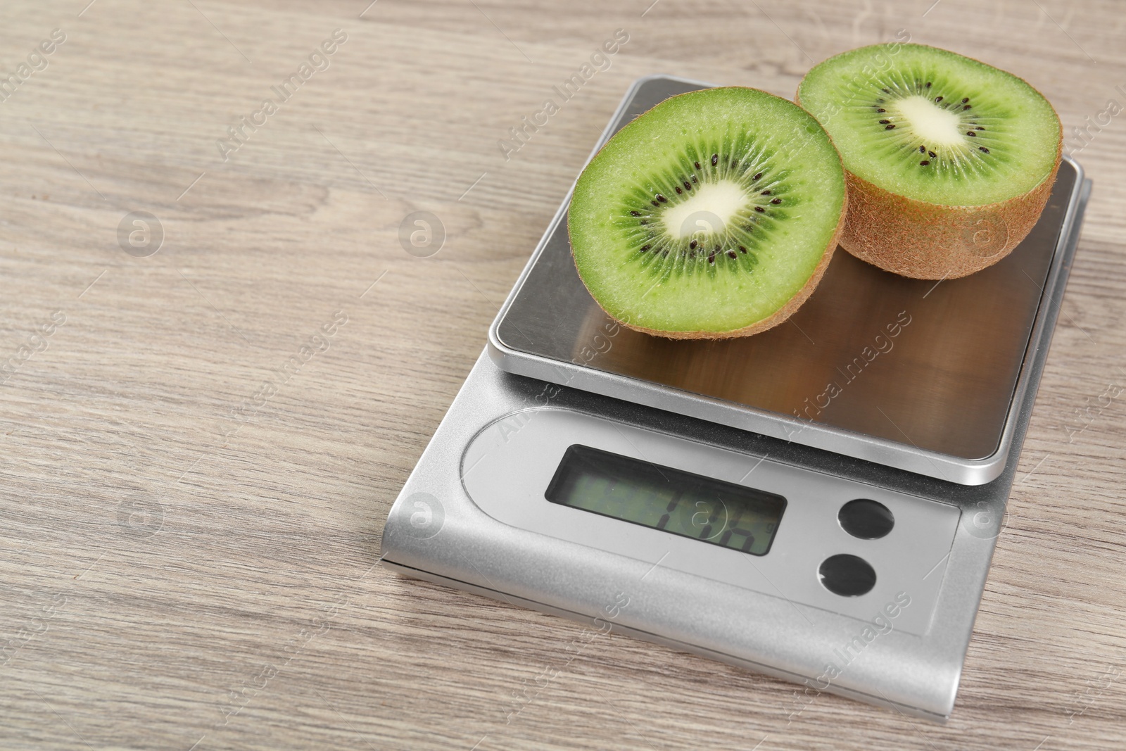 Photo of Kitchen scale with halves of kiwi on light wooden table, closeup. Space for text