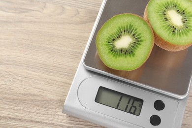 Kitchen scale with halves of kiwi on light wooden table, closeup. Space for text