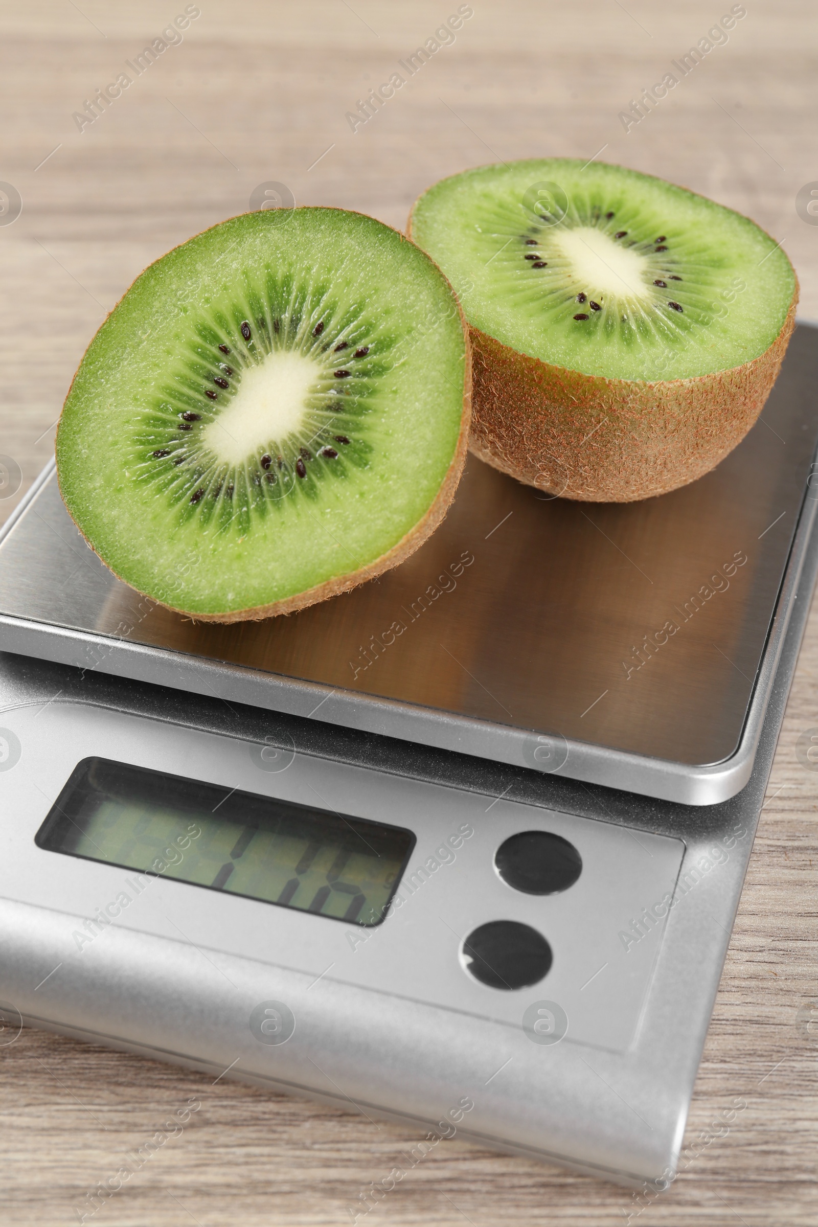 Photo of Kitchen scale with halves of kiwi on light wooden table, closeup