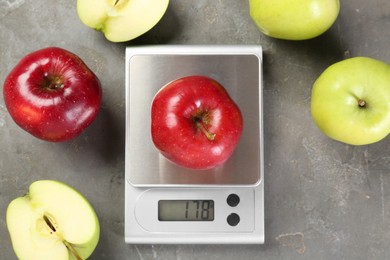 Kitchen scale with apple among ones on grey textured table, flat lay