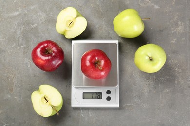 Photo of Kitchen scale with apple among ones on grey textured table, flat lay