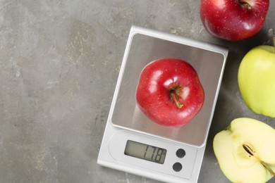 Kitchen scale with apple among ones on grey textured table, flat lay. Space for text