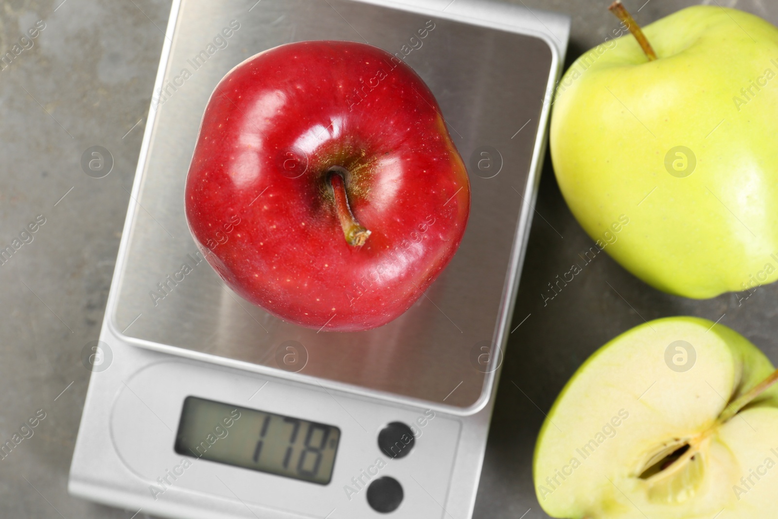 Photo of Kitchen scale with apple among ones on grey textured table, flat lay