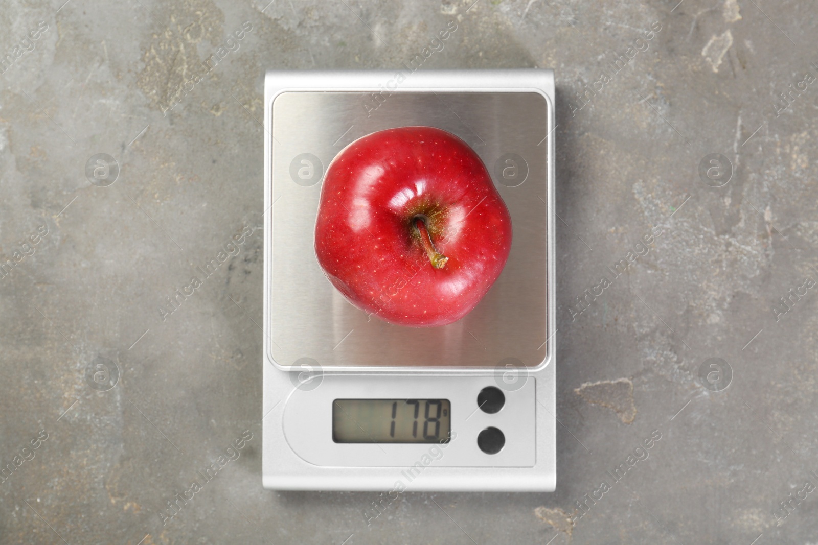 Photo of Kitchen scale with apple on grey textured table, top view