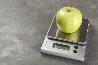 Kitchen scale with apple on grey textured table, closeup. Space for text