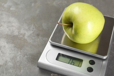 Photo of Kitchen scale with apple on grey textured table, closeup. Space for text