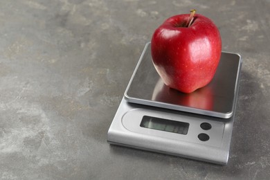 Photo of Kitchen scale with apple on grey textured table, closeup. Space for text