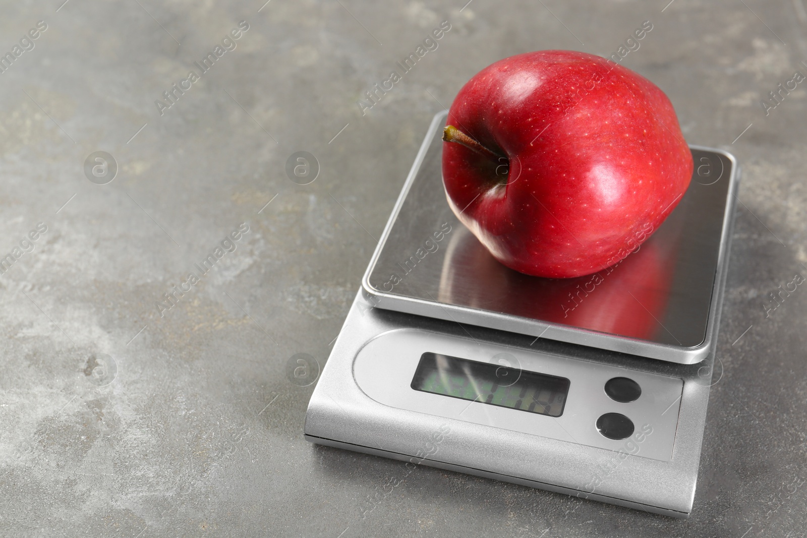 Photo of Kitchen scale with apple on grey textured table, closeup. Space for text