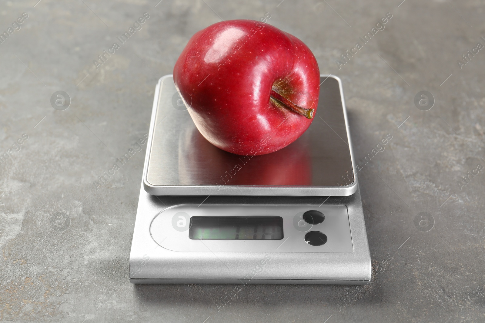 Photo of Kitchen scale with apple on grey textured table, closeup