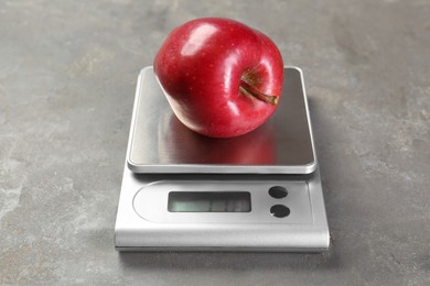 Photo of Kitchen scale with apple on grey textured table, closeup