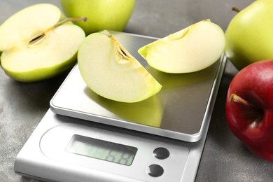 Kitchen scale with pieces of apple and fruits on grey textured table, closeup