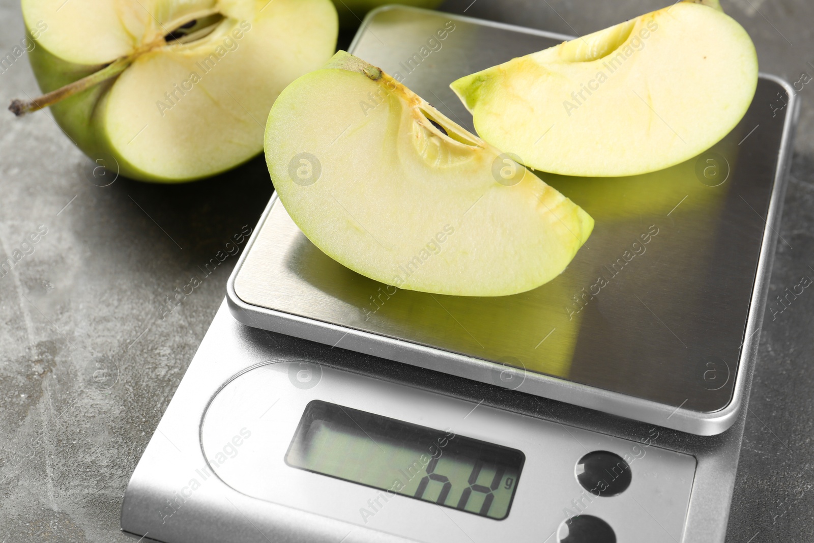 Photo of Kitchen scale with pieces of apple and fruits on grey textured table, closeup