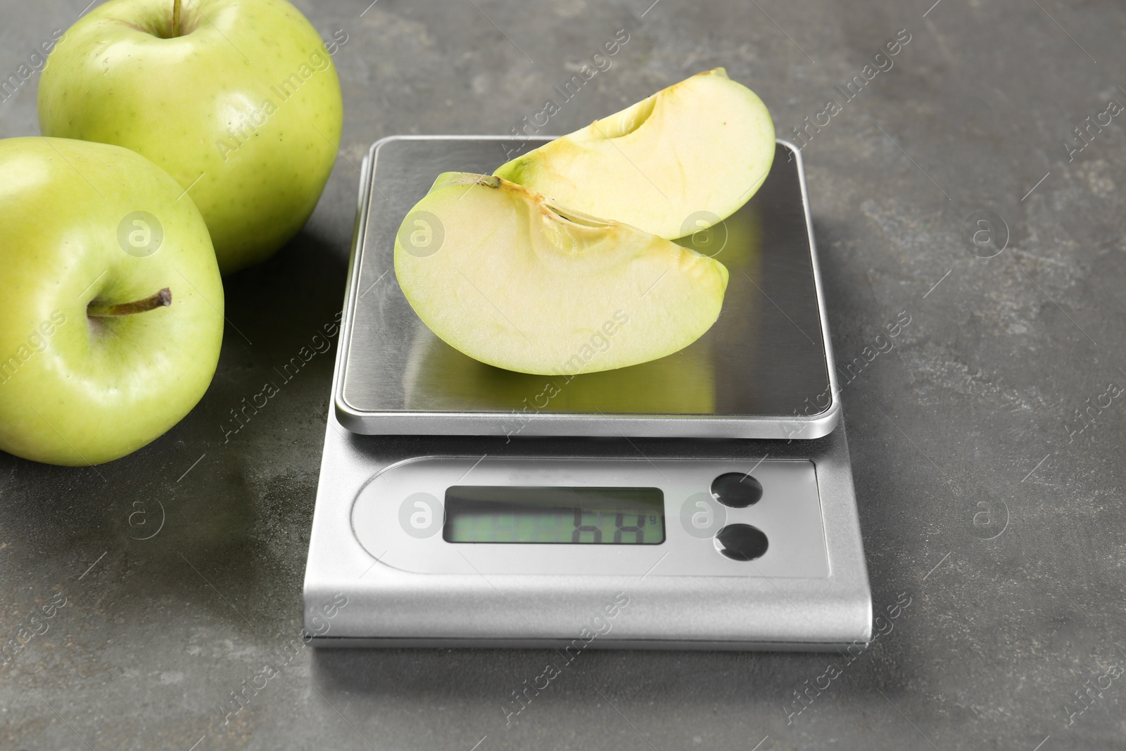 Photo of Kitchen scale with pieces of apple and fruits on grey textured table, closeup