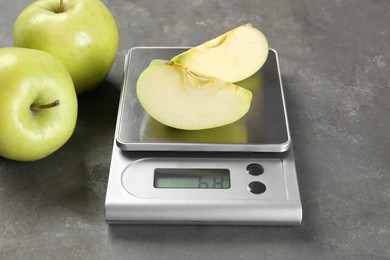 Kitchen scale with pieces of apple and fruits on grey textured table, closeup